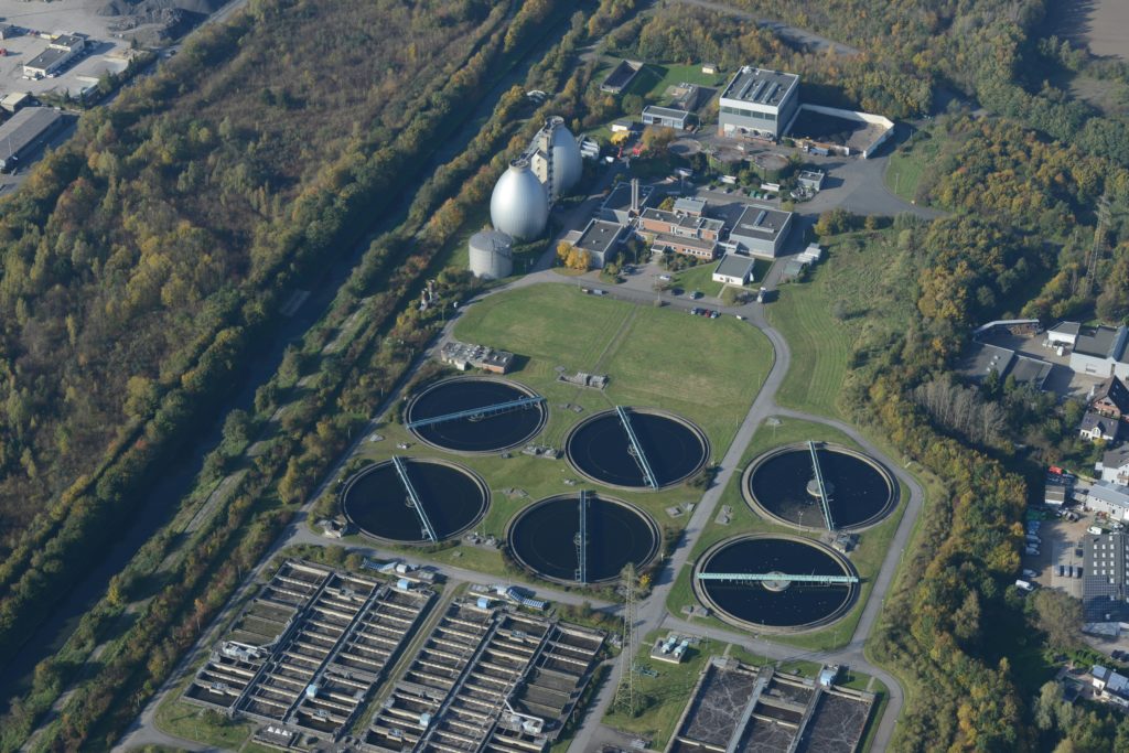 Aerial photograph of a wastewater treatment plant surrounded by autumn trees, showcasing ecological and industrial elements.